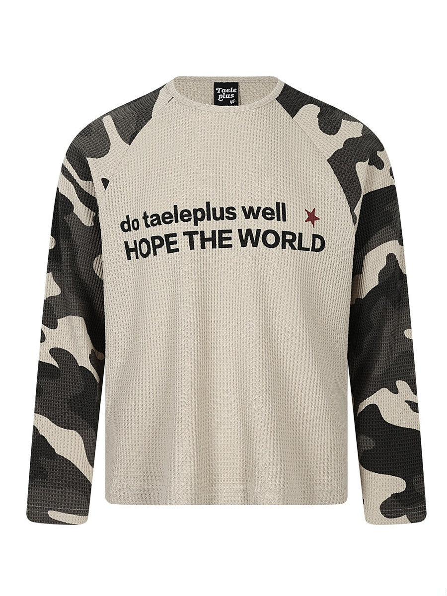 ベージュのワッフル長袖Tシャツ。袖は迷彩柄のラグランで、胸に英字スローガンのプリント