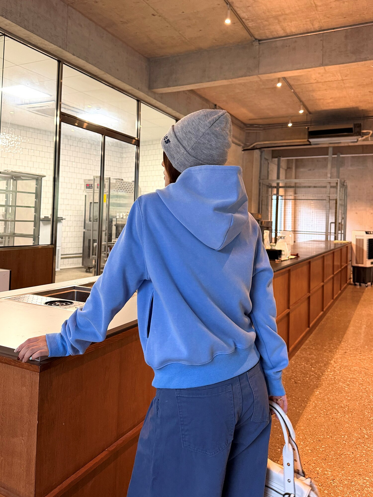 ブルーのミリタリー調ジップパーカーの後ろ姿。フード付きで裾はリブ