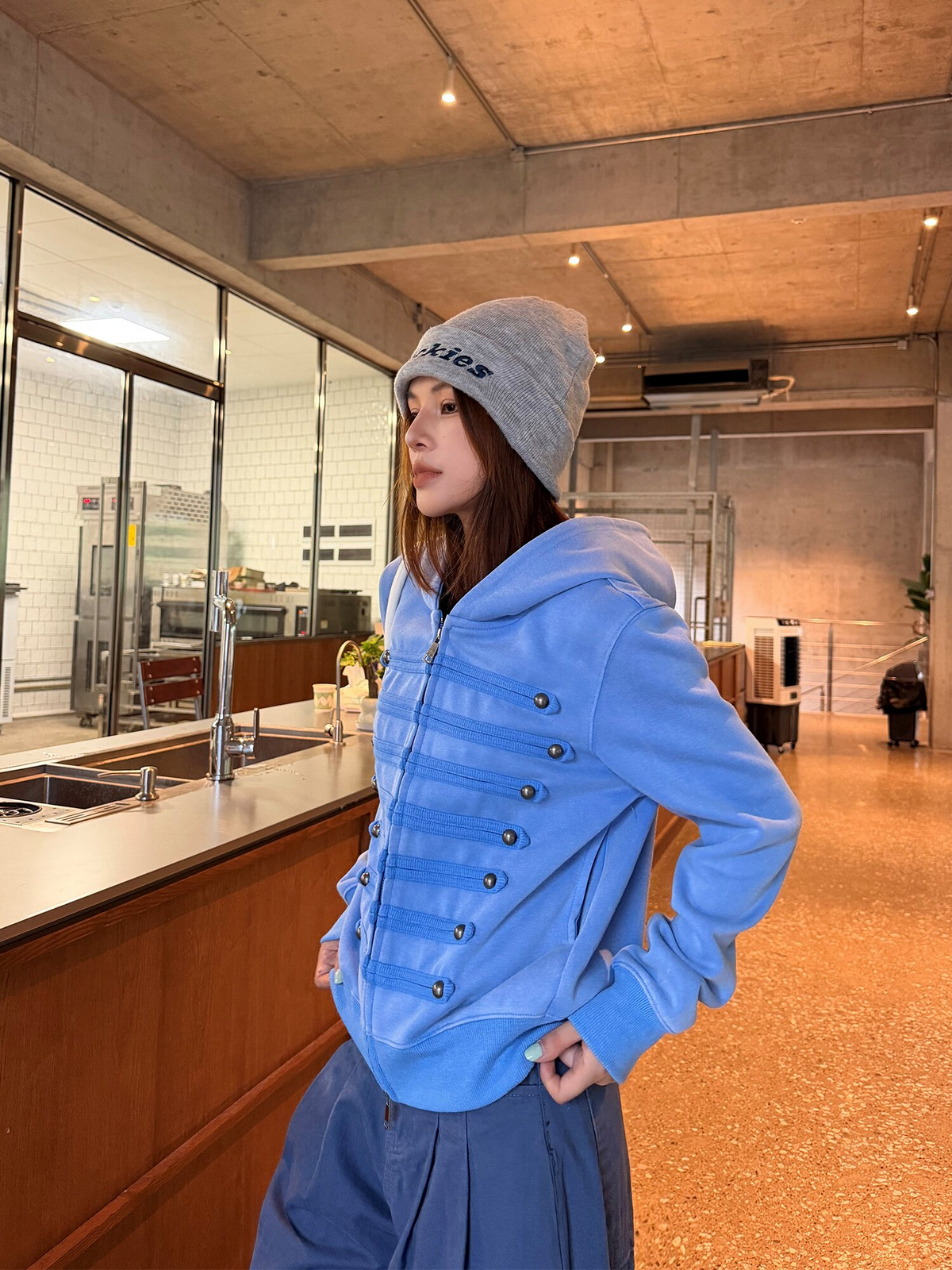 ブルーのミリタリー調ジップパーカーの着用。体を斜めに向けた上半身で、飾り紐と袖の幅が分かる