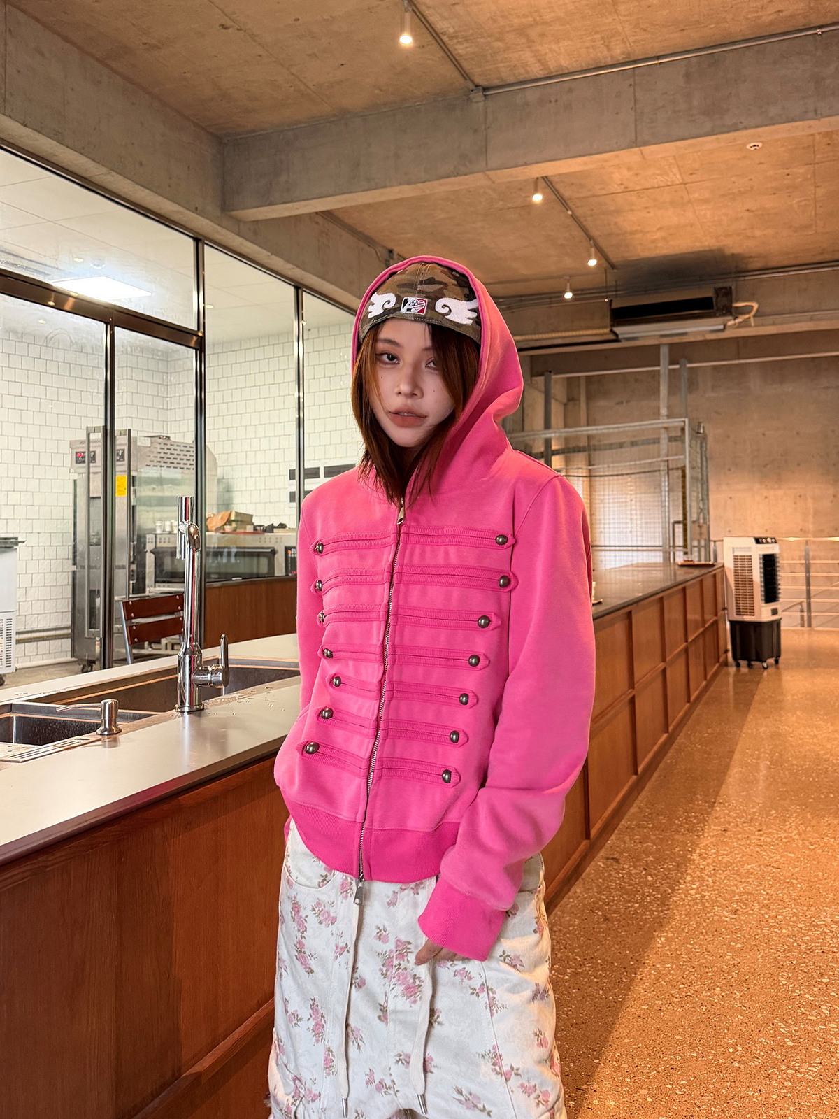 ホットピンクのミリタリー調ジップパーカーをフードをかぶって着用。正面の上半身